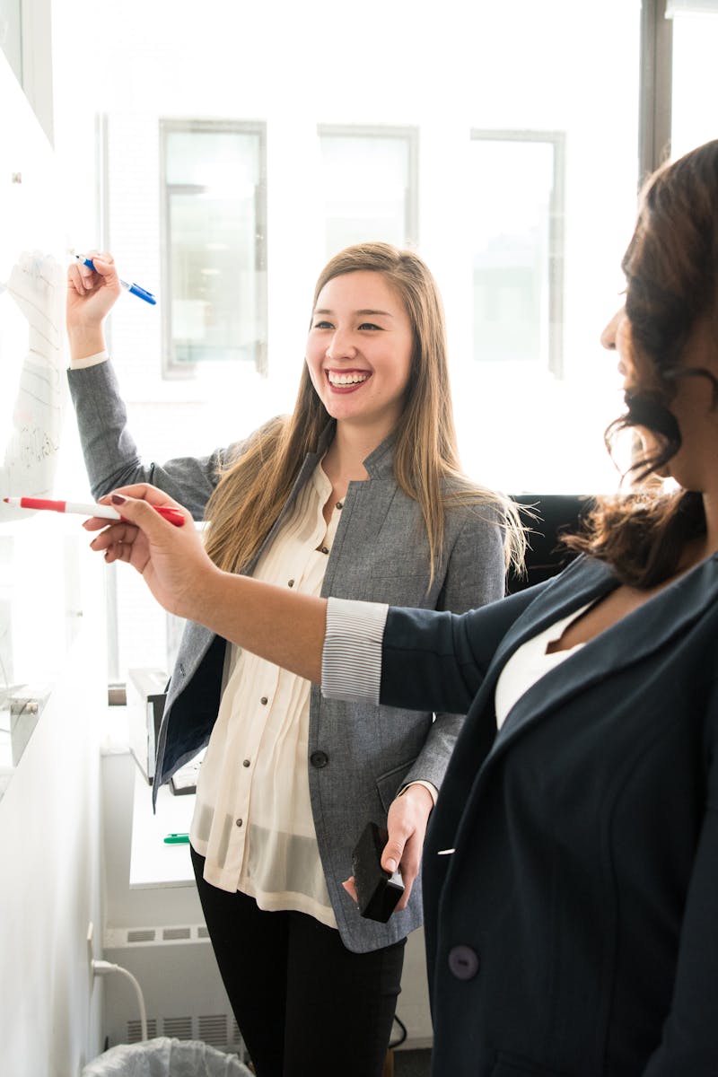 Two professional women discussing ideas on a whiteboard in a modern office setting.
